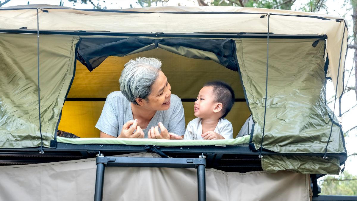 a grandmother and her grandson camping together, looking at each other and smiling